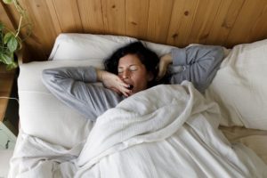 Woman with eyes closed yawning in bed at home